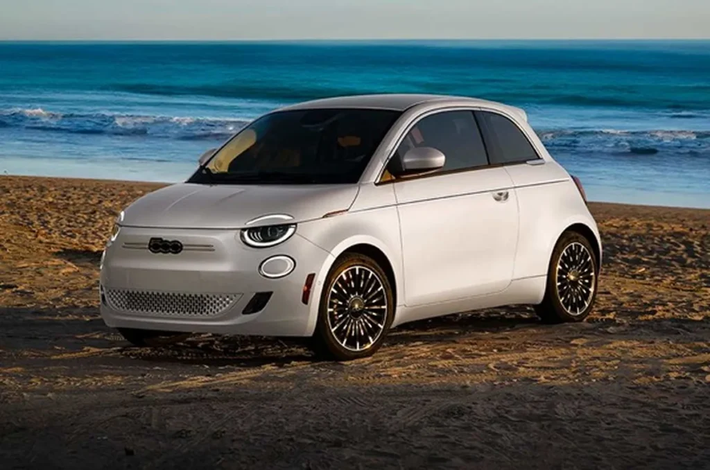 A white Fiat 500e parked on a scenic coastal road with the ocean in the background.